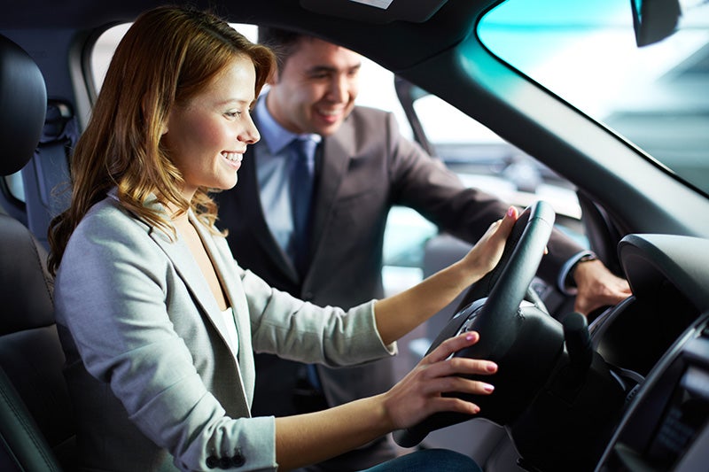 salesperson showing feature to woman who is sitting n driving seat