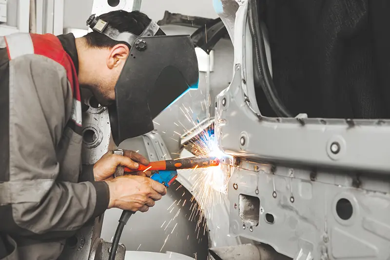 Worker welding a car frame with safety gear 